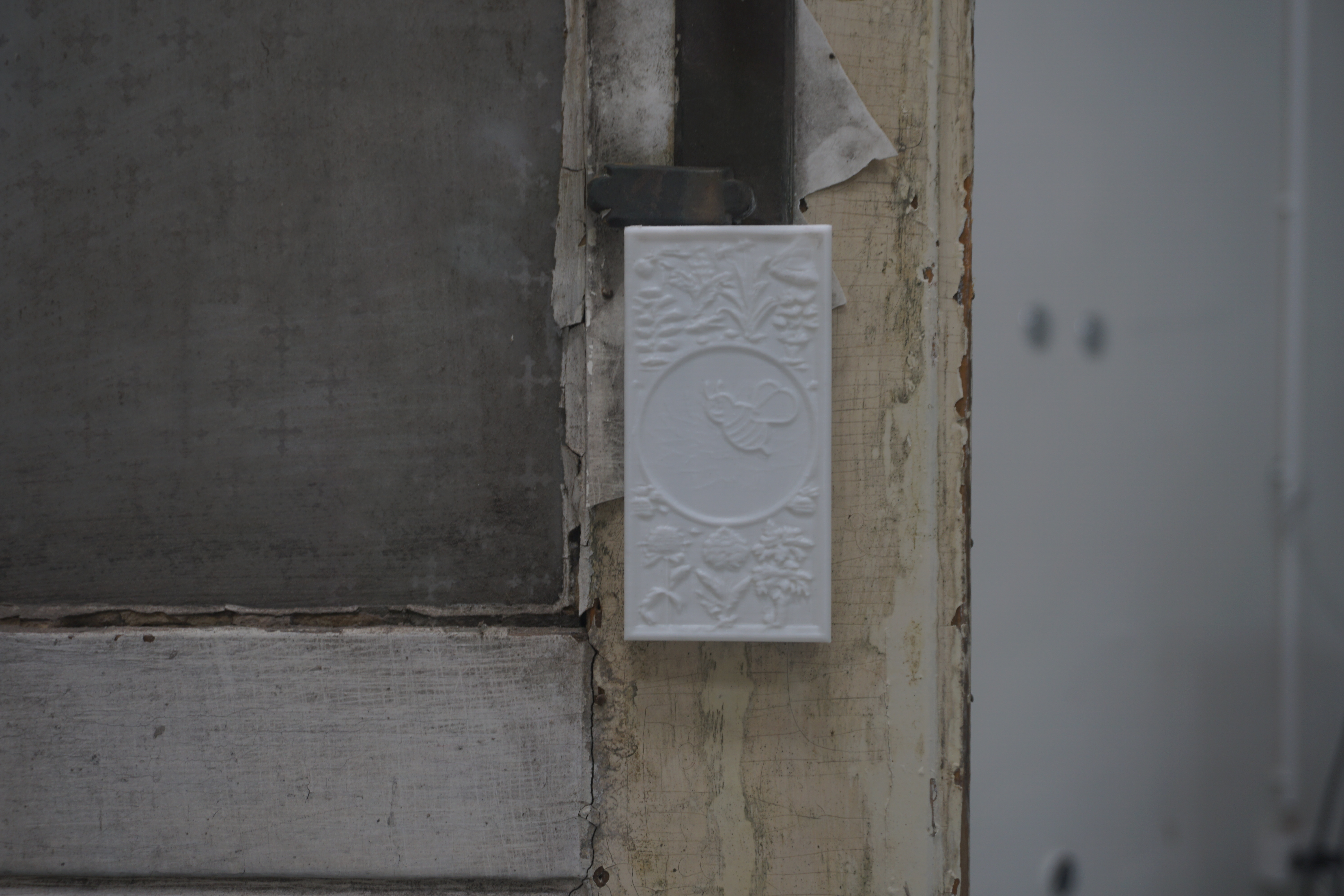 Detail of a white relief plaque with a bee surrounded by flowers, mounted on the frame of an old painted door