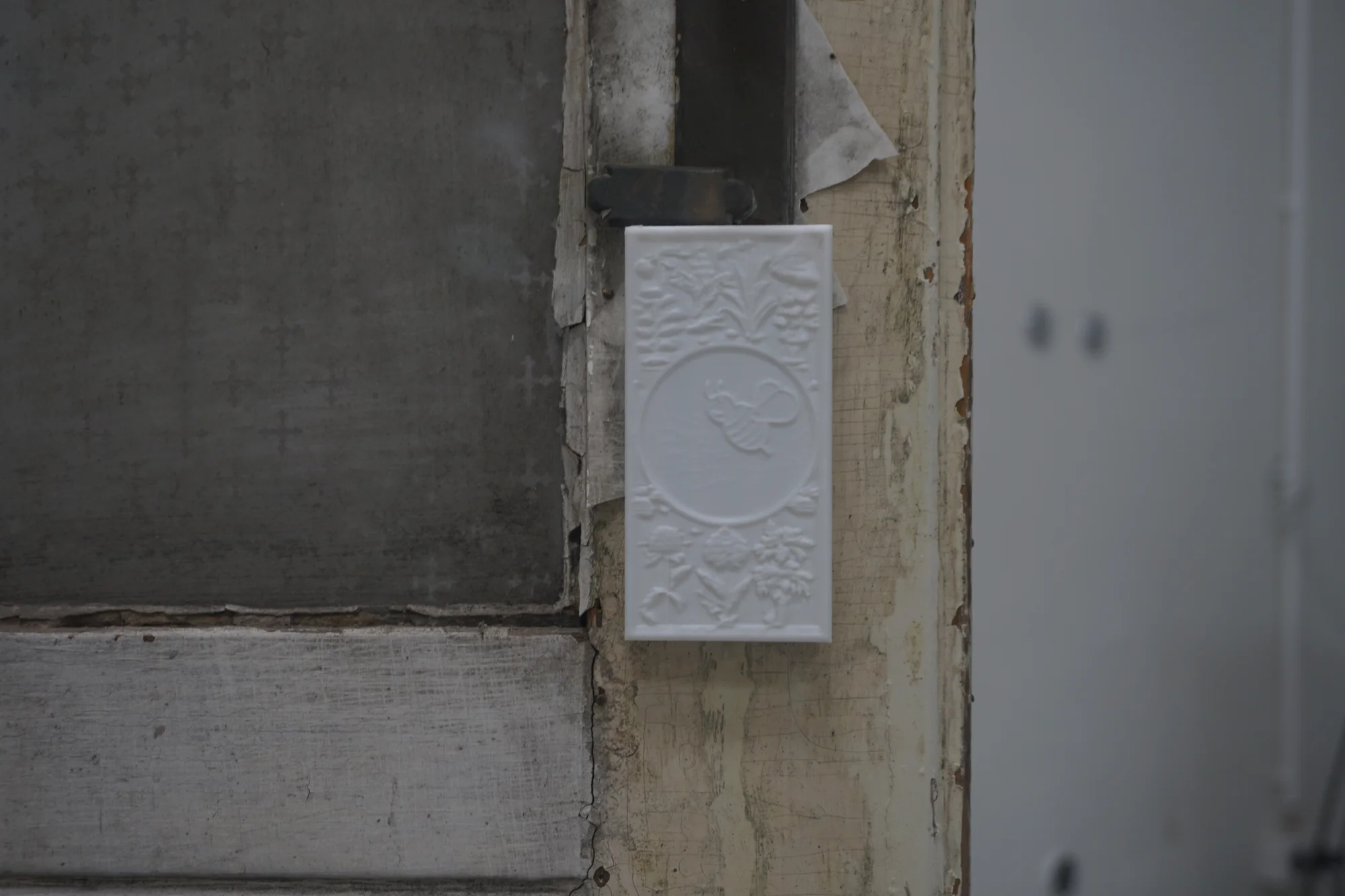 Detail of a white relief plaque with a bee surrounded by flowers, mounted on the frame of an old painted door